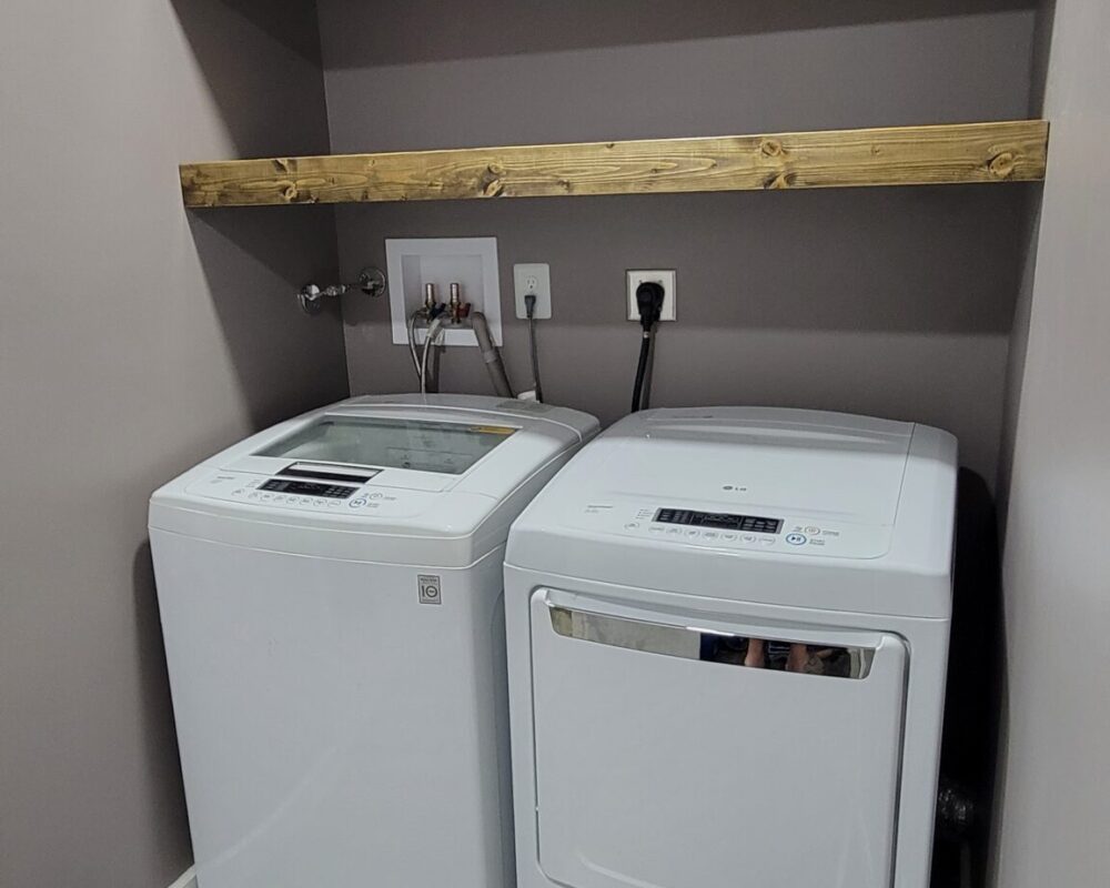 Washer and dryer appliances in a modern laundry area with a wooden shelf above, showcasing home renovation and design by TurnKey Builds in South Florida.