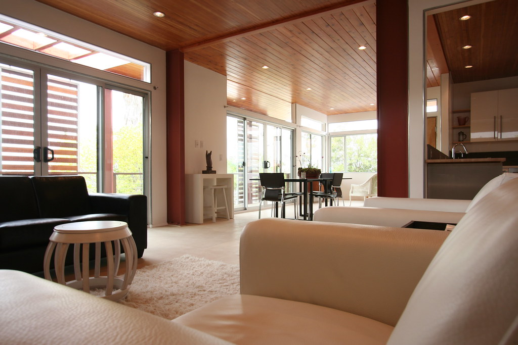 Modern living room featuring a black sofa, white accent chairs, and a round coffee table, with large windows allowing natural light, emphasizing a spacious, open design ideal for home remodeling inspiration in South Florida.