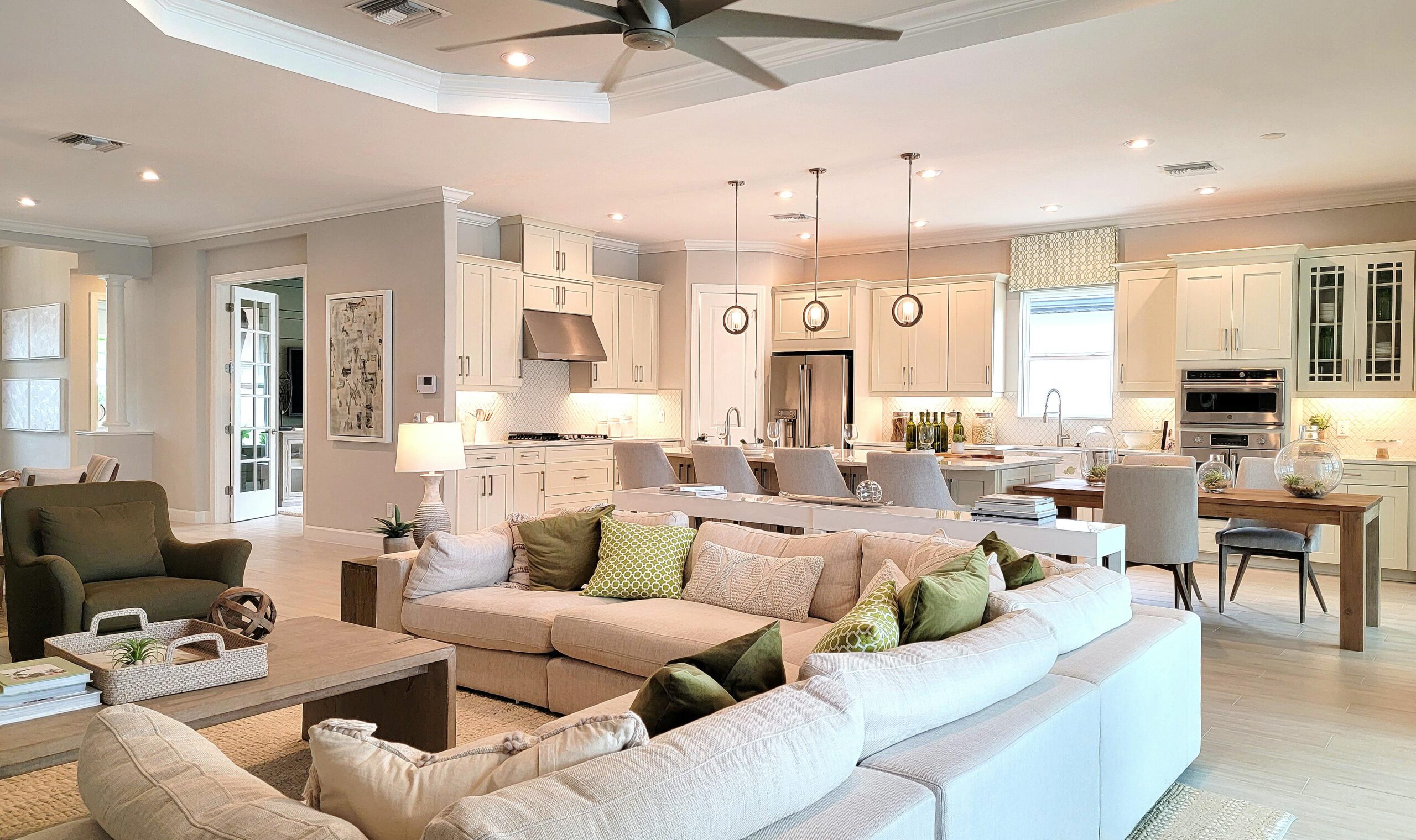 Spacious modern living area featuring a light-filled kitchen with custom cabinetry, quartz countertops, and stylish pendant lighting, complemented by a cozy sectional sofa and green accent pillows, showcasing a recent home renovation by TurnKey Builds in South Florida.