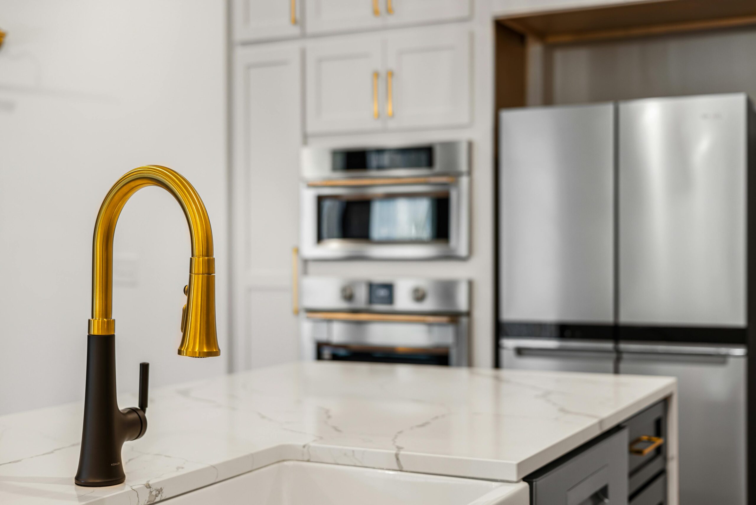 Modern kitchen with white cabinetry, stainless steel appliances, and gold faucet.