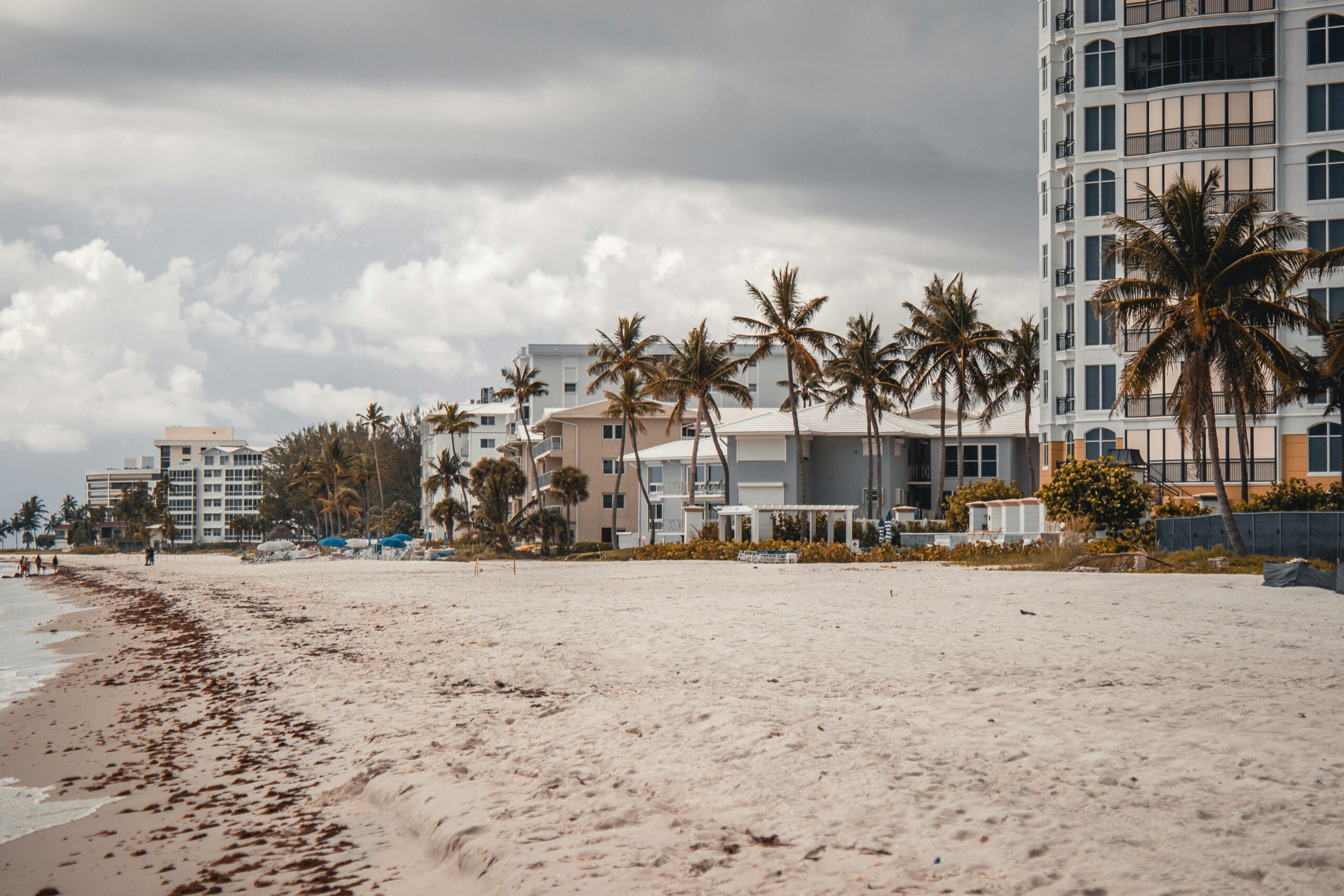 Pompano Beach shoreline with luxury condos, palm trees, and sandy beach under cloudy skies, reflecting the upscale coastal environment targeted by Turnkey Builds for home renovations.