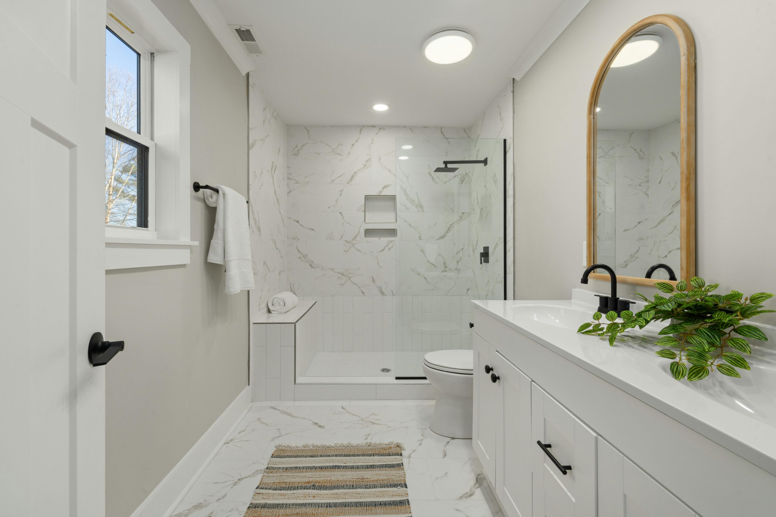 Modern bathroom featuring a walk-in rain shower with glass enclosure, double floating vanity with black fixtures, heated tile floors, and a large backlit mirror, emphasizing luxury design elements for a spa-like experience.