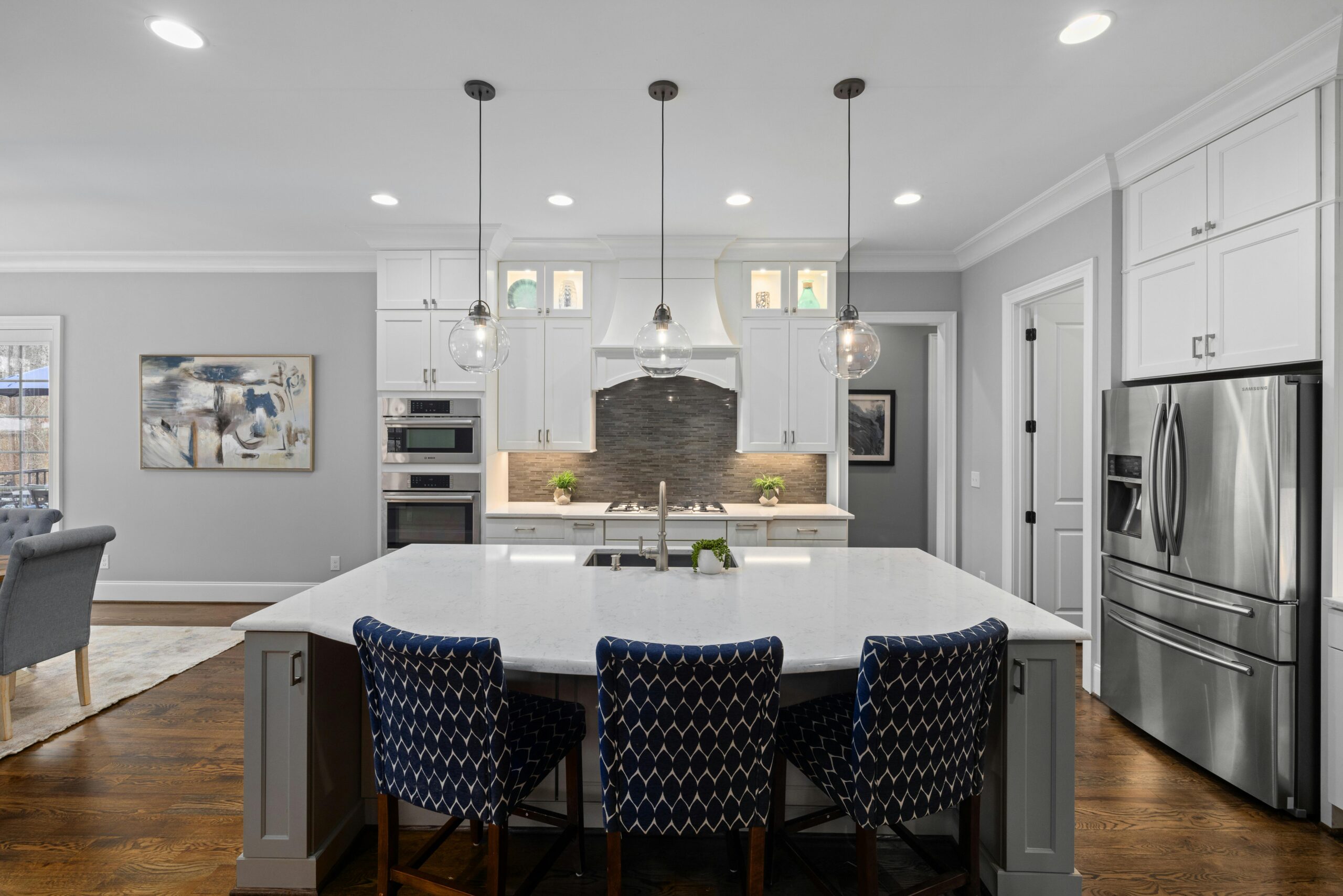 Modern kitchen with white cabinetry, quartz countertop, stainless steel appliances, and stylish pendant lighting over a large island with blue patterned stools, showcasing a contemporary design ideal for kitchen remodels.