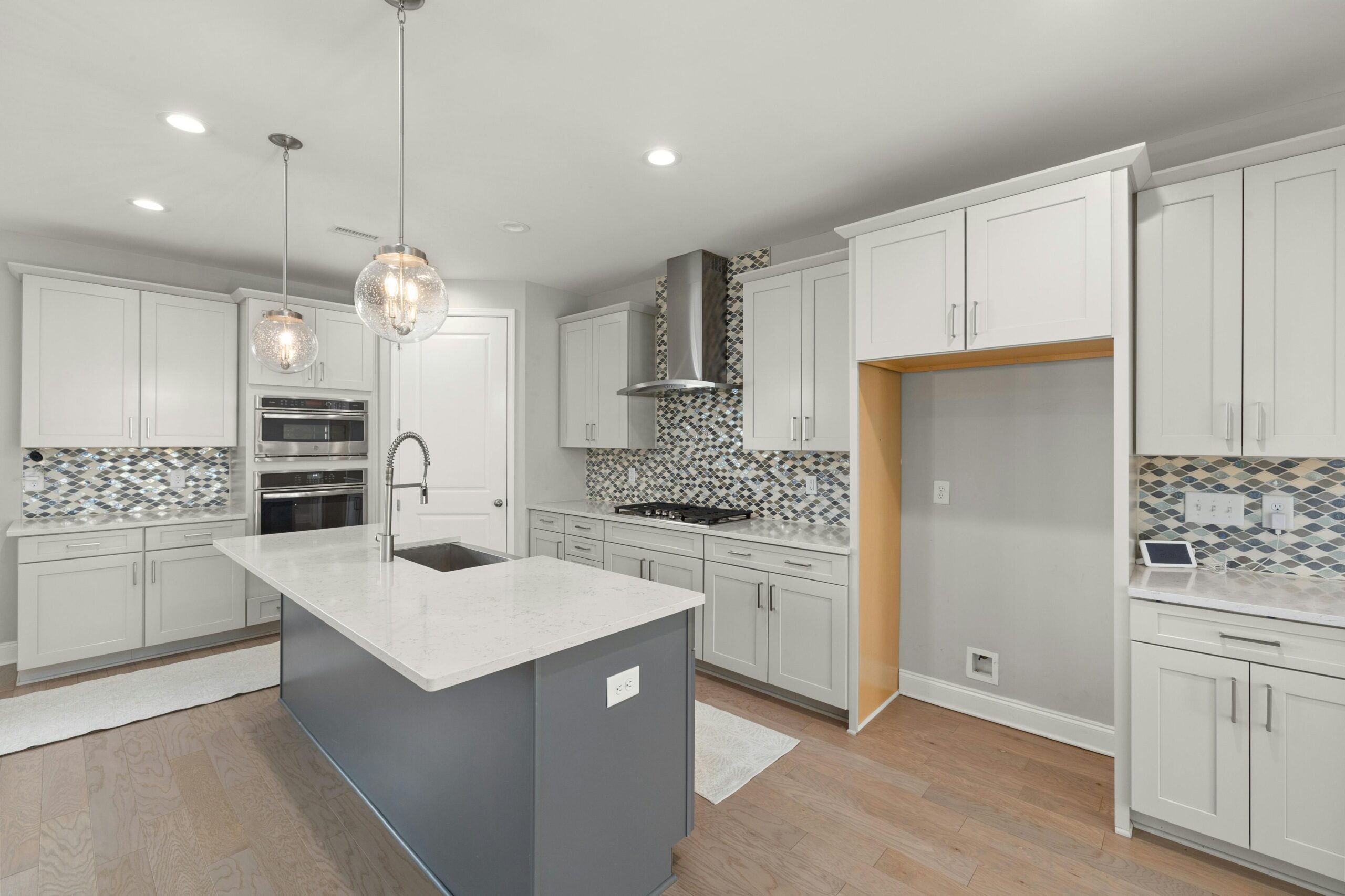 Modern kitchen featuring all-white custom cabinetry, mosaic tile backsplash, stainless steel appliances, and a contrasting gray center island with undermount sink, showcasing a bright and contemporary design ideal for high-end renovations.