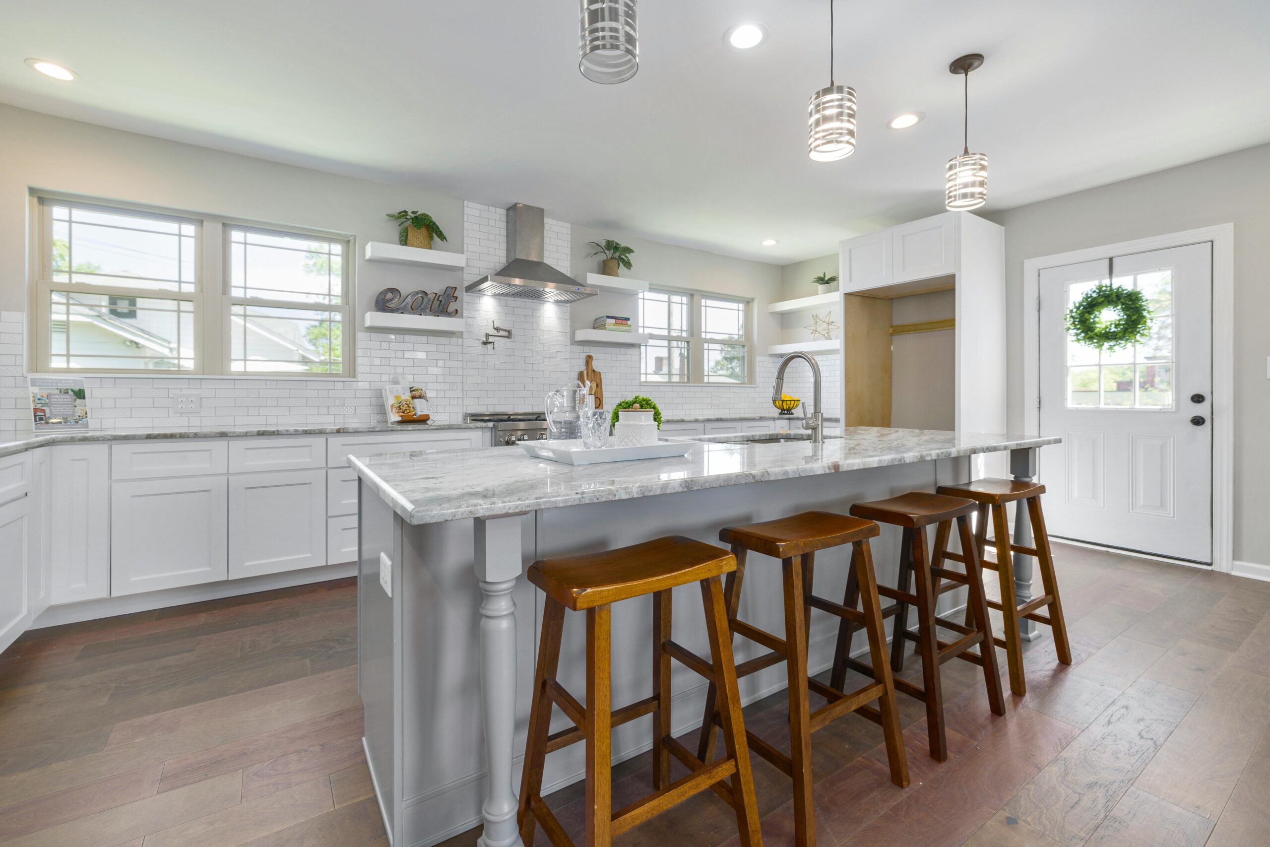 Modern kitchen interior featuring white cabinetry, granite countertop, and stainless steel appliances, complemented by wooden bar stools and natural light from windows, ideal for home remodeling showcases.
