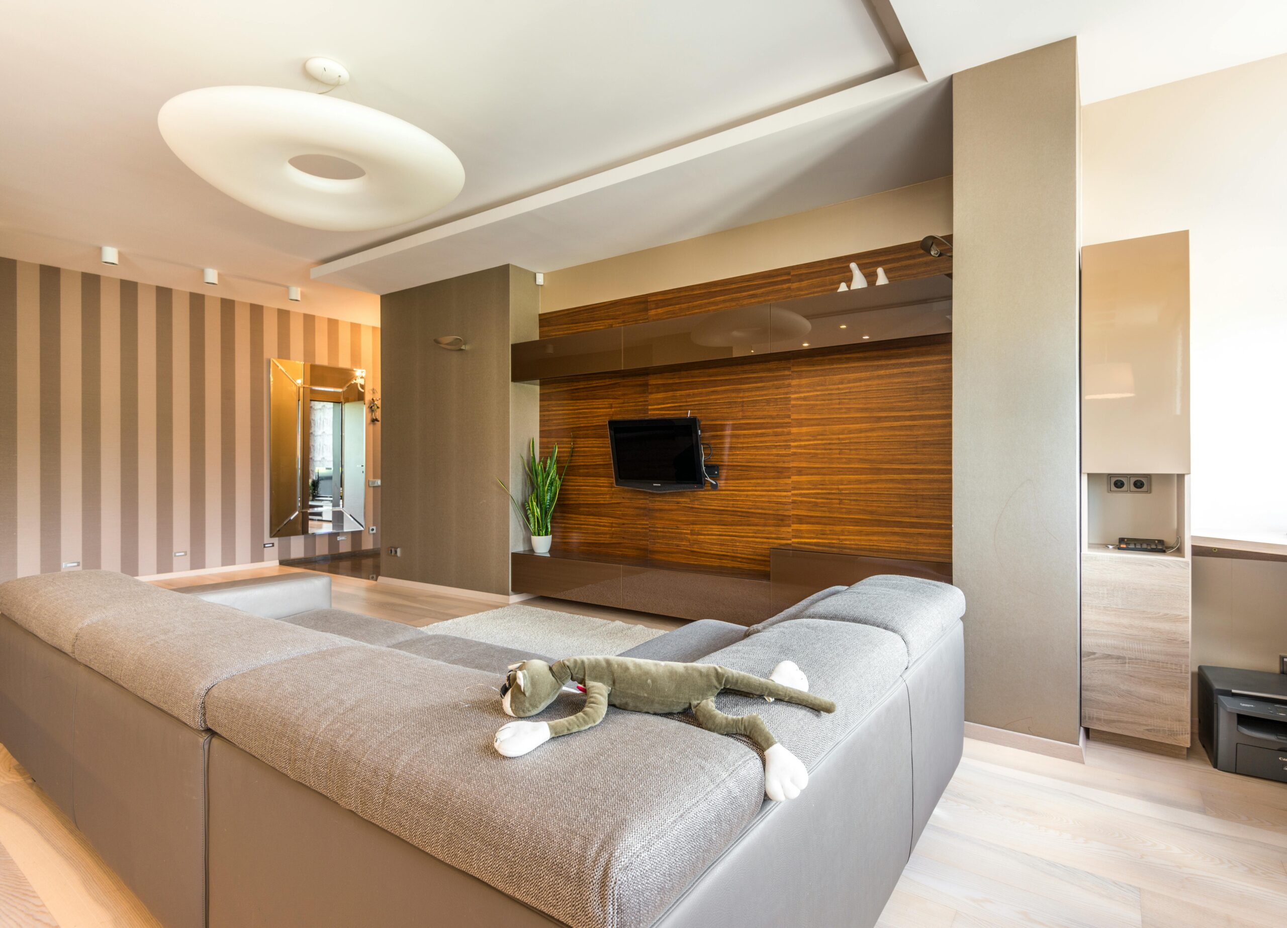 Modern living room featuring a sleek sectional sofa, contemporary decor, a flat-screen TV mounted on a wooden accent wall, and a decorative plant, emphasizing premium craftsmanship and design suitable for South Florida homeowners.