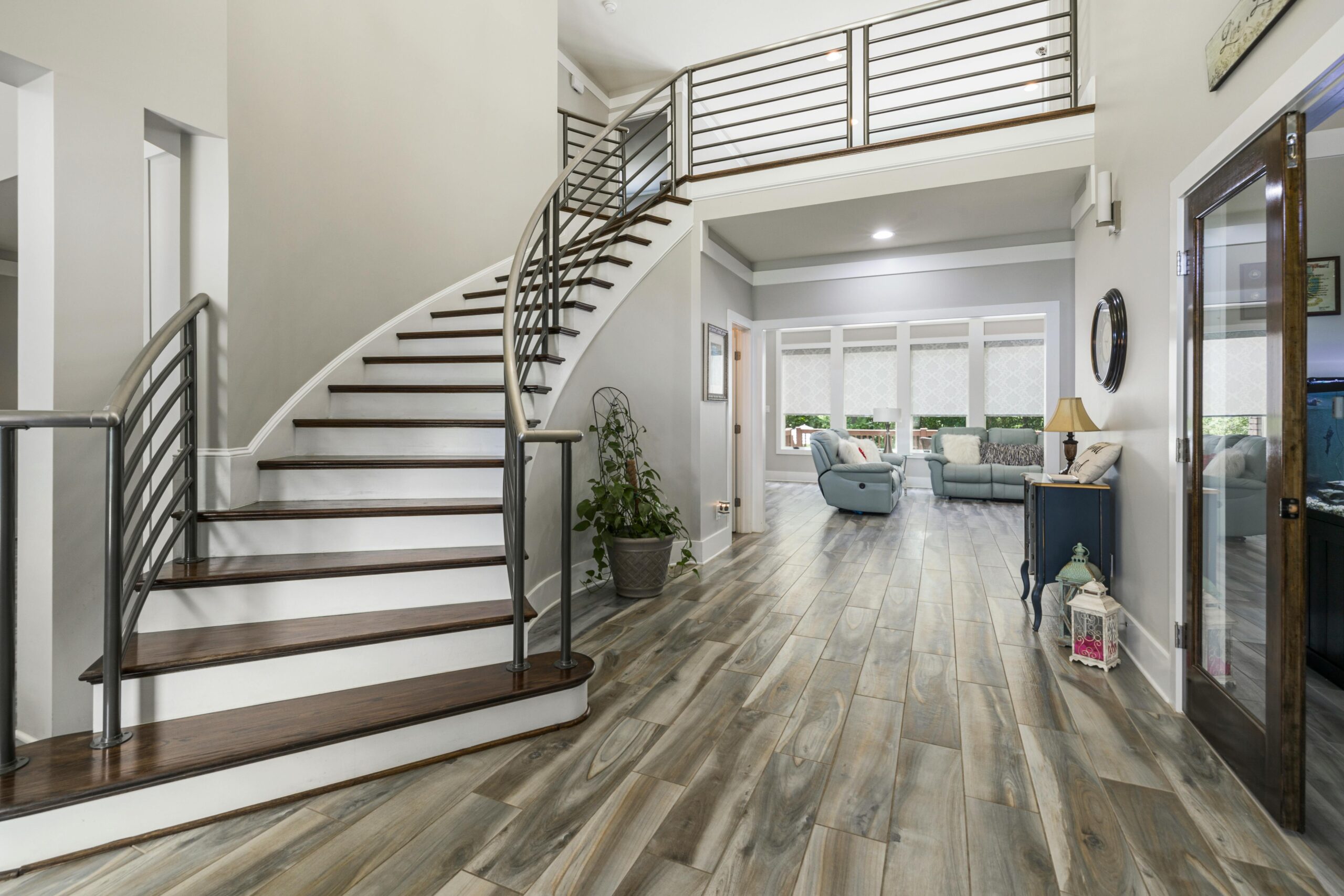 Modern entryway featuring a curved staircase, stylish railing, and wooden flooring, leading to a spacious living area with comfortable seating and natural light, showcasing TurnKey Builds' interior renovation expertise for North Miami homes.