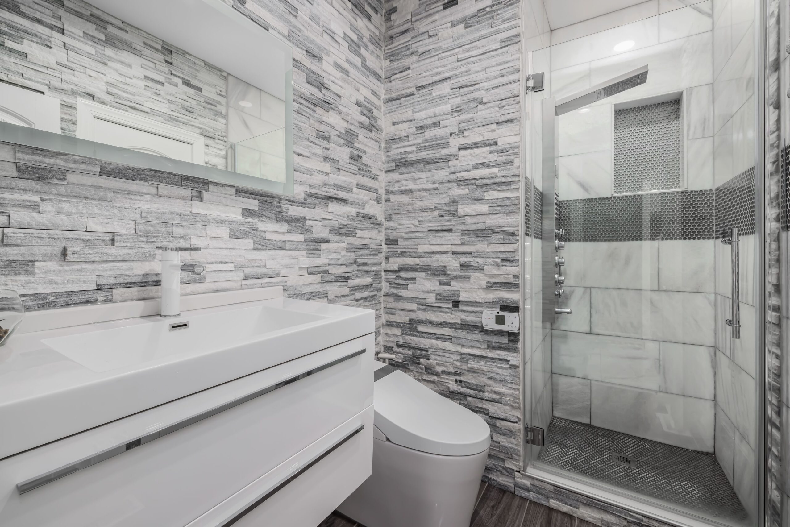 Modern bathroom remodel with gray tile shower and white vanity.