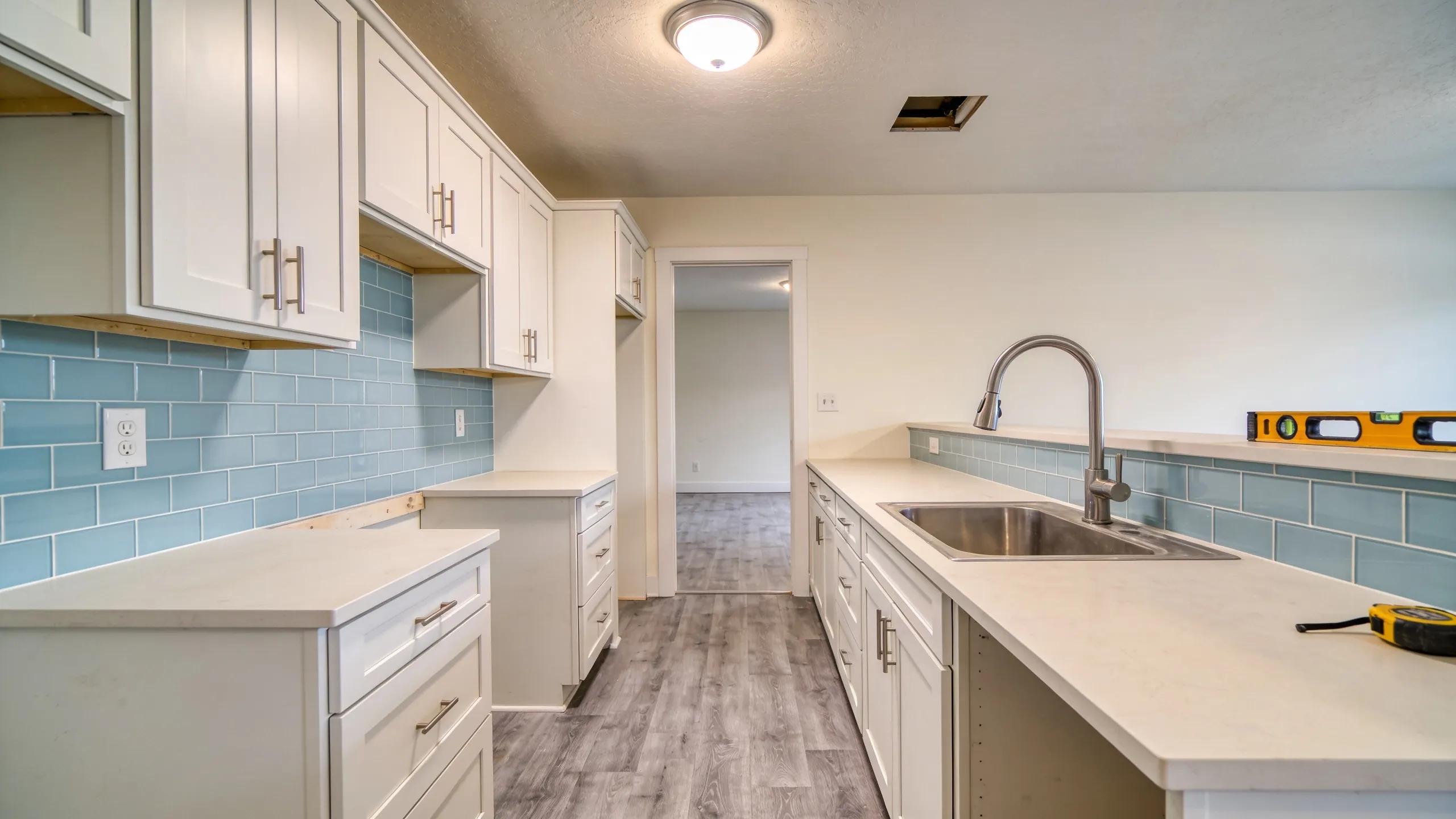 Kitchen remodel in progress with white cabinetry, blue tile backsplash, and stainless steel sink.